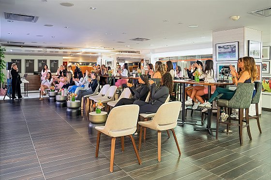 Large indoor event space with numerous attendees seated and standing throughout a modern venue with contemporary furniture and gallery-style artwork on walls.