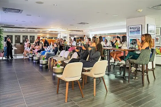 Large indoor event space with numerous attendees seated and standing throughout a modern venue with contemporary furniture and gallery-style artwork on walls.