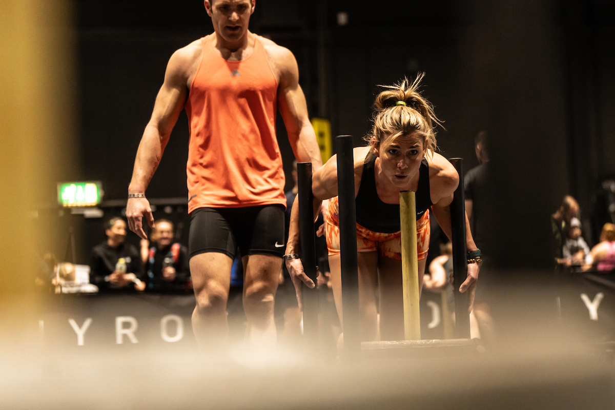 Athlete pushing a weighted sled during a HYROX fitness challenge event, showcasing functional fitness, strength, endurance, and competitive race training.