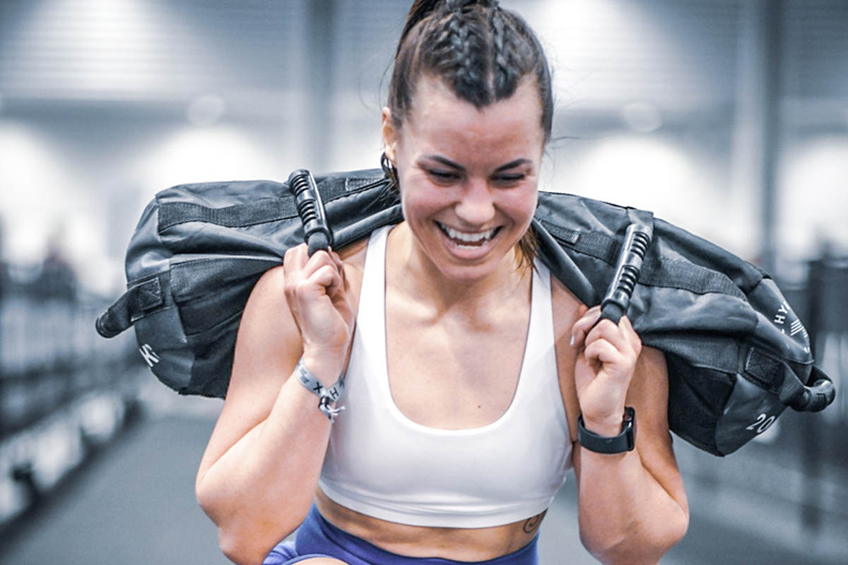 Athlete carrying a weighted sandbag during a HYROX fitness challenge event, showcasing functional strength, endurance, and race-specific training.