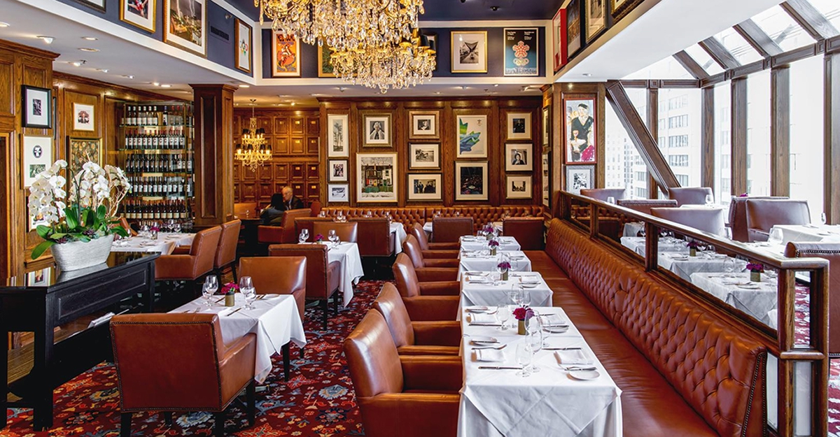 An elegant dining room with leather seating, chandeliers, and framed artwork on the walls.