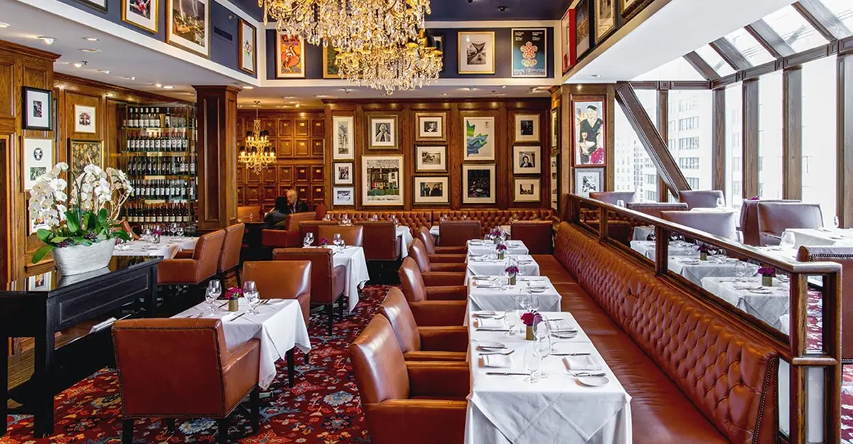 An elegant dining room with leather seating, chandeliers, and framed artwork on the walls.
