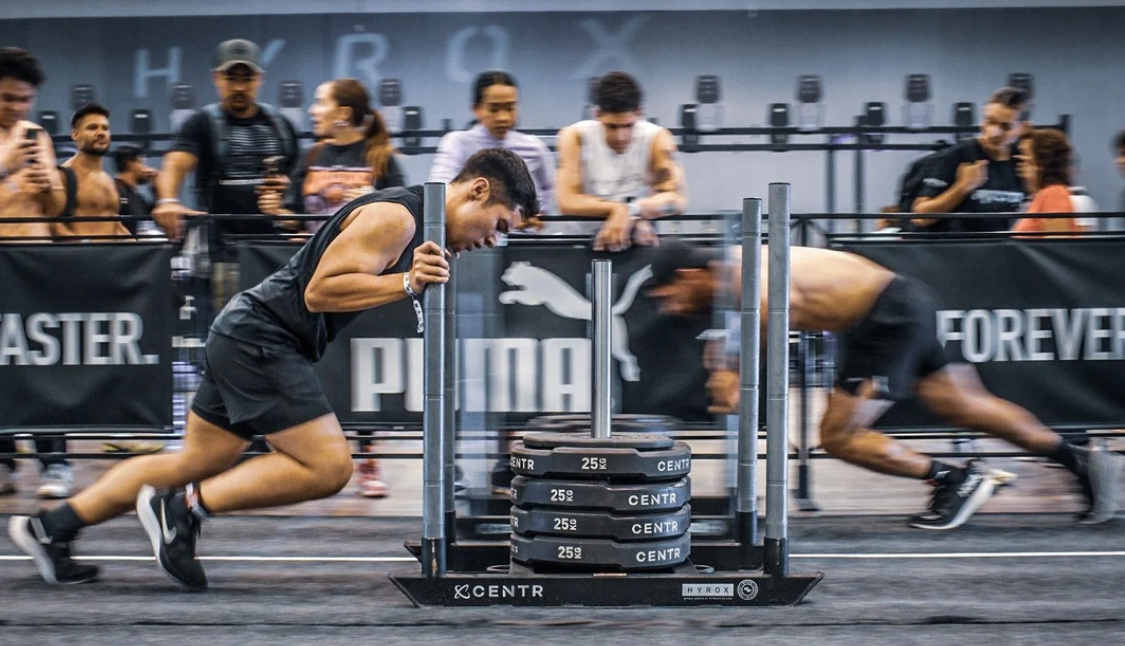 Competitors completing the HYROX sled push station in a HYROX fitness race event.