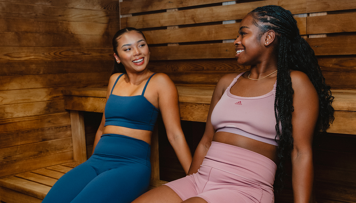 Two people sitting together in a sauna, smiling and talking after a workout.