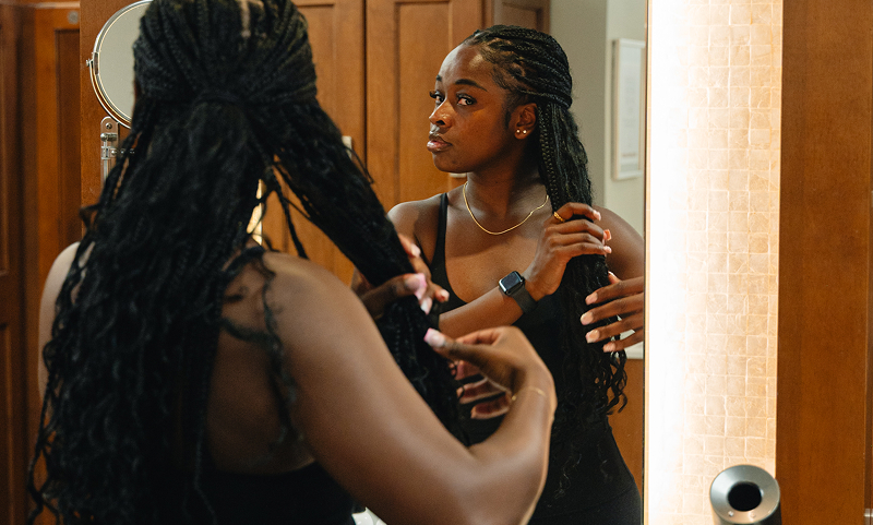 A woman styling her hair in the Adelaide Club locker room, standing at a mirror with warm wooden lockers behind her.
