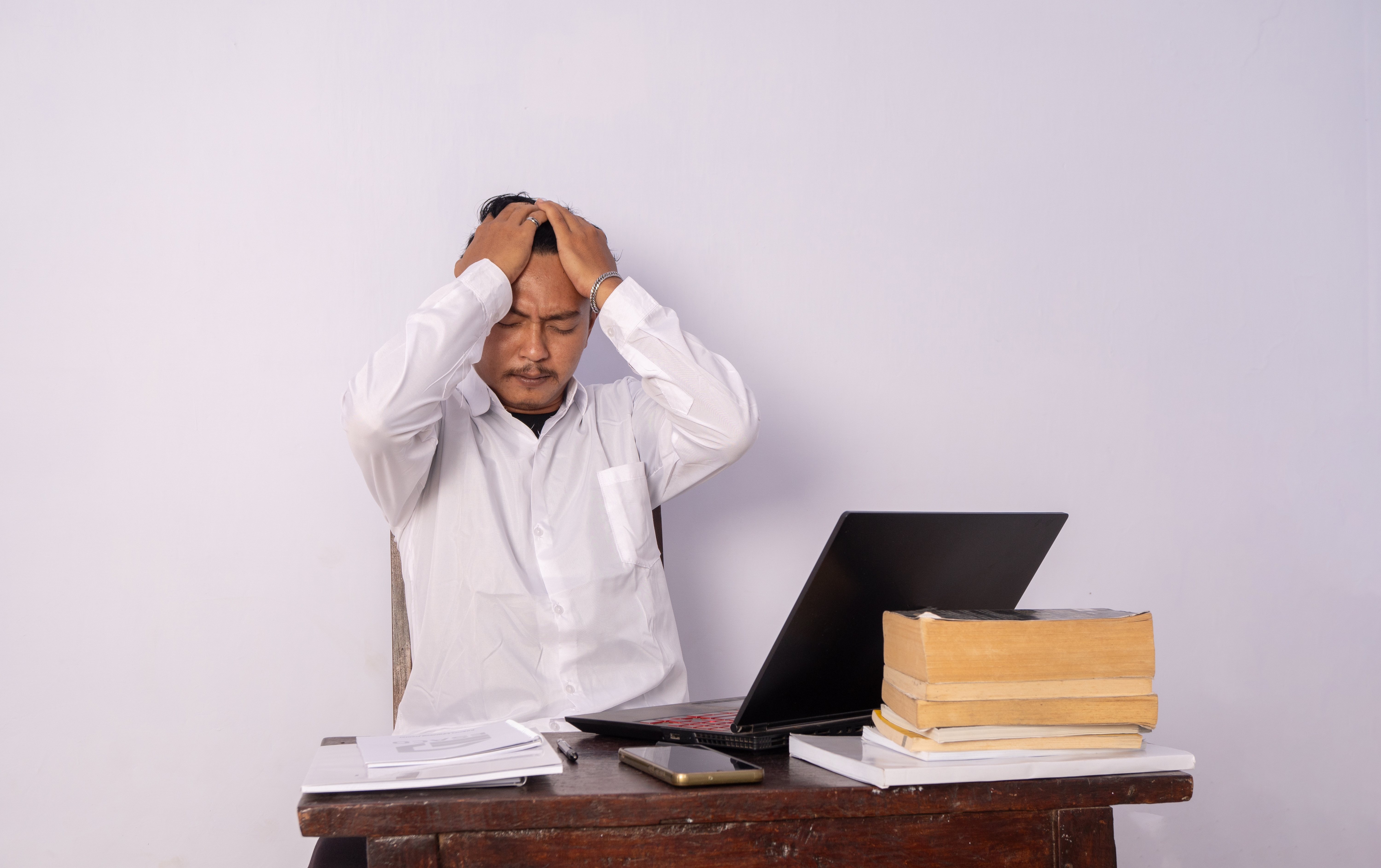 Man with his head in his hands sitting at his desk Man with his head in his hands sitting at his desk