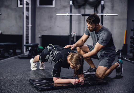 Young male trainer working with a female client that is doing a plank on the gym floor