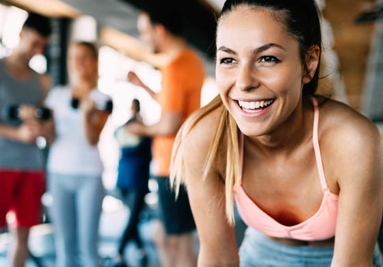 Close-up of young, fit woman smiling with men and women working out in the background