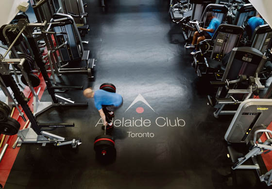 Camera shooting from above - male trainer down in the Build Gym at the Adelaide Club completing deadlift on top of the Adelaide Club logo on the ground