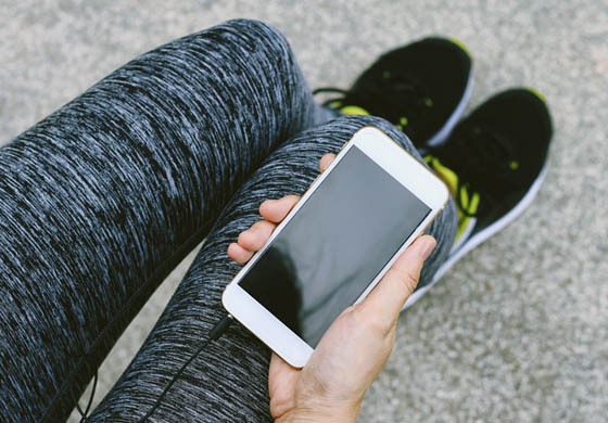 Close-up of the hand and legs of a woman in athletic gear, holding her phone - screen facing up - in her hand