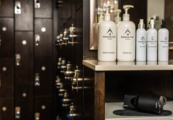 Body lotion, hand soap, hair dryer, and other amenities on the vanity in the men's locker room at the Adelaide Club, with dark wood lockers in the background
