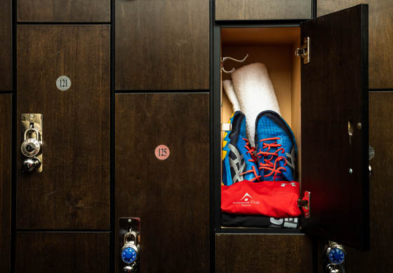 Close-up of a locker in the men's locker room at the Adelaide Club with a towel rolled up in the back and blue and red squash shoes, red t-shirt, and black shorts folded near the front
