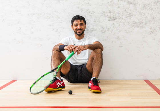 Young man sitting on the squash court smiling, holding a squash racquet